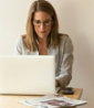 woman wearing grey striped dress shirt sitting down near brown wooden table in front of white laptop computer